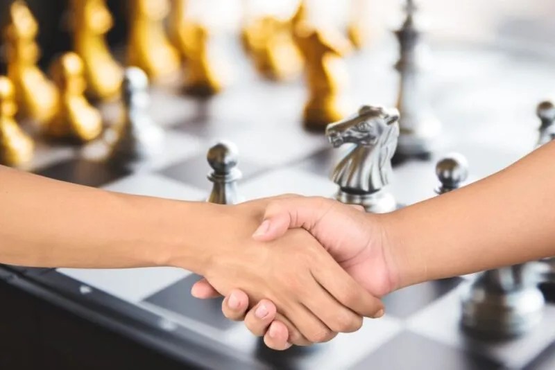 Los peones se odian entre sí, mientras los jugadores del tablero sonríen y mueven las piezas